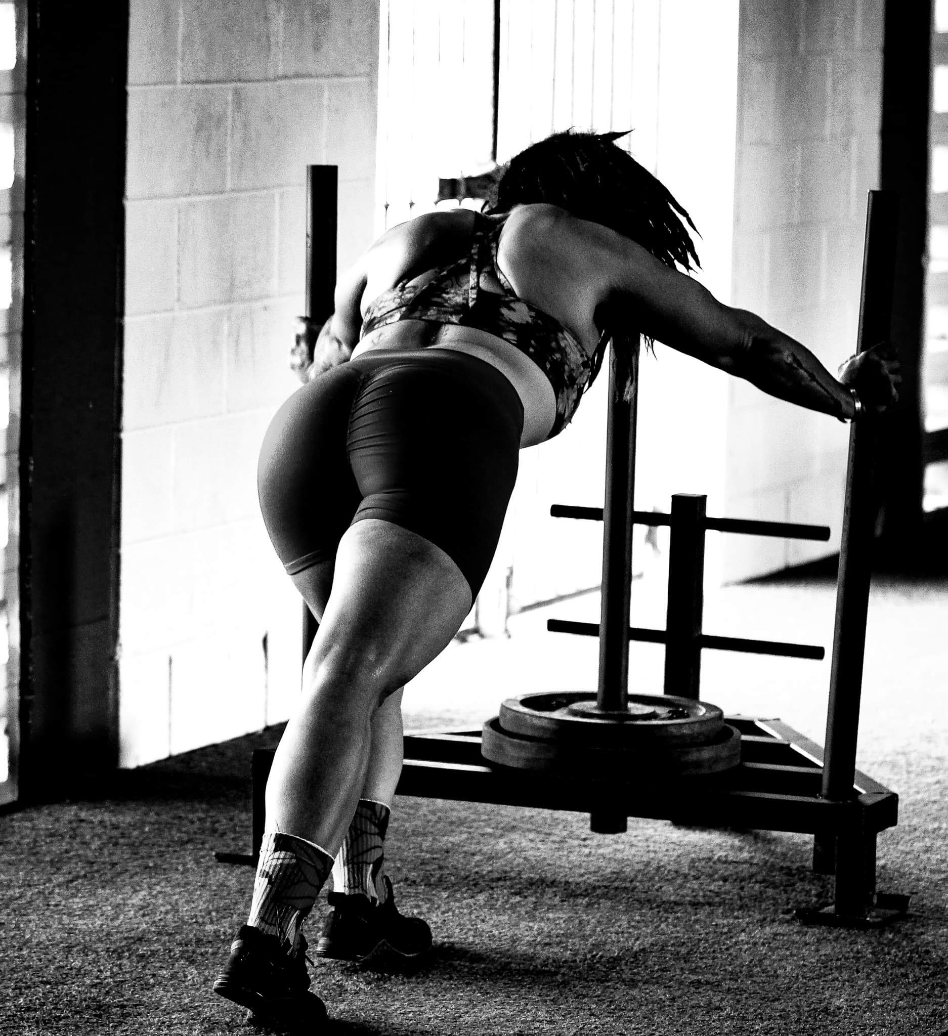 Member driving a loaded sled across the gym floor while others train behind