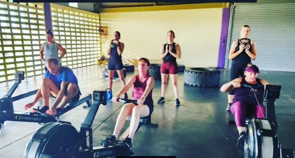 Small group working on rowing machines and bikes with a coach nearby