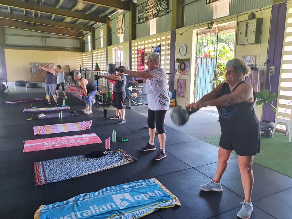 Older members swinging kettlebells in a bright group session