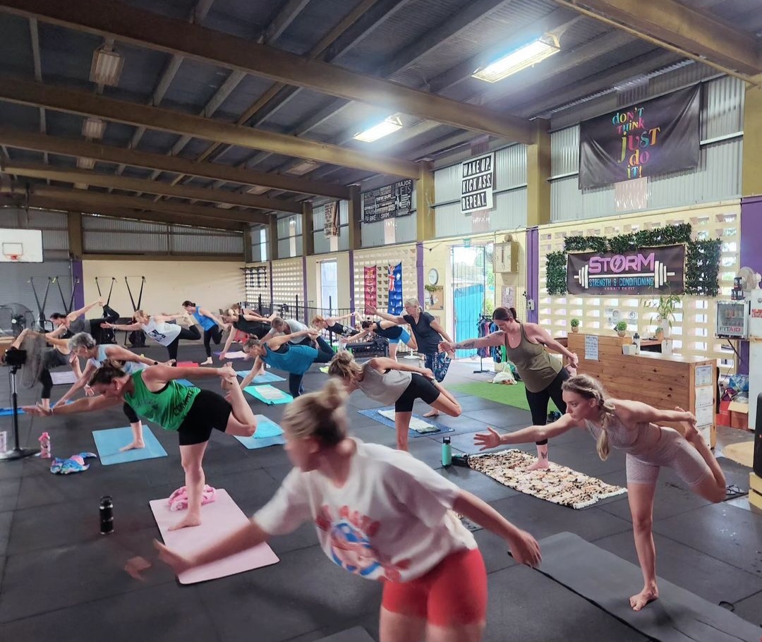 Mat Pilates class stretching side by side on mats under the shed roof