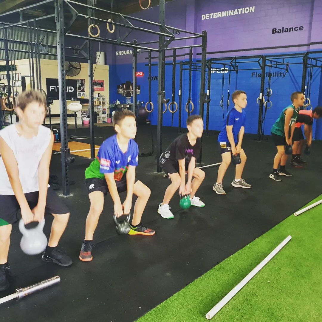Teenagers lifting kettlebells side by side with a coach supervising